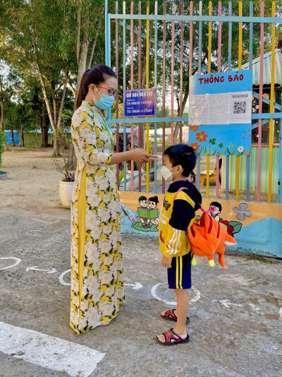Giáo viên đo thân nhiệt cho bé trước khi vào lớp.